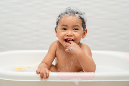 happy infant baby take a bath and playing with foam bubbles in bathtub at homeの写真素材