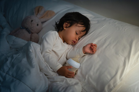 toddler baby sleeping on a bed after drinking milk bottle at nightの写真素材