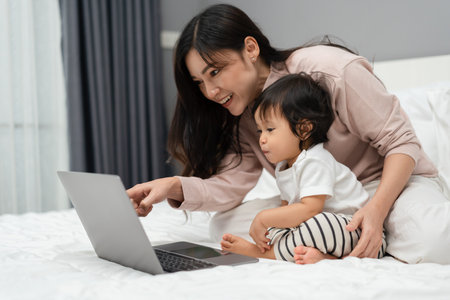 toddler baby with mother using and watching laptop computer on a bedの写真素材