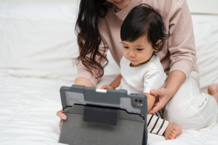 toddler baby with mother using digital tablet pc on a bedの写真素材