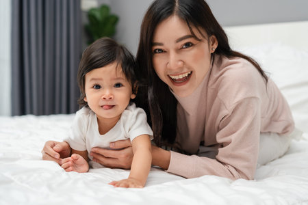 happy mother lying and playing with her infant baby on a bedの写真素材