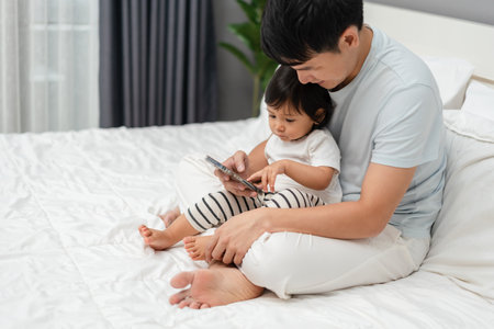 toddler baby with father using smartphone on a bedの写真素材
