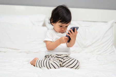 toddler baby using and watching smartphone on a bedの写真素材
