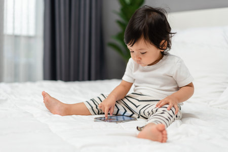 toddler baby using smartphone on a bedの写真素材