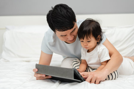 toddler baby with father looking digital tablet pc on a bedの写真素材