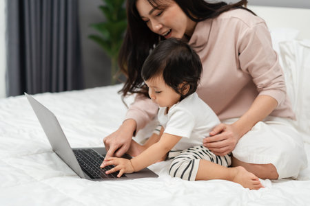 toddler baby with mother using and typing on laptop computer on a bedの写真素材