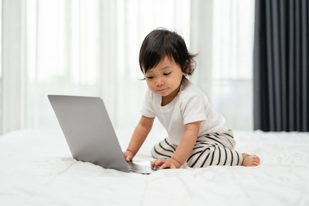 toddler baby using laptop computer on a bedの写真素材
