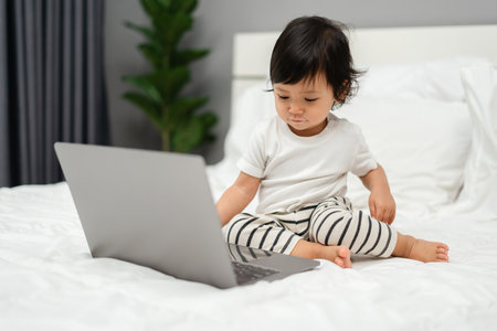 toddler baby watching laptop computer on a bedの写真素材