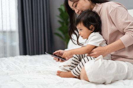 toddler baby with mother using smartphone on a bedの写真素材