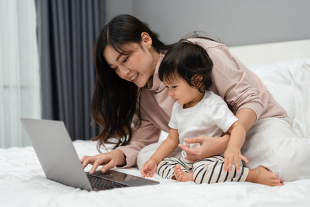 toddler baby with mother using laptop computer on a bedの写真素材