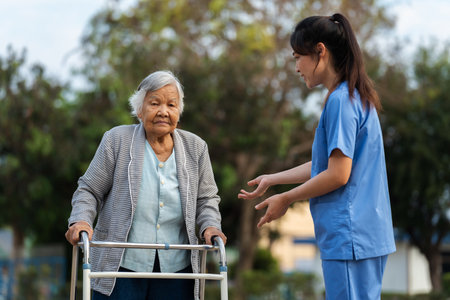 caregiver nurse is teaching senior woman to walk with walker at the parkの写真素材