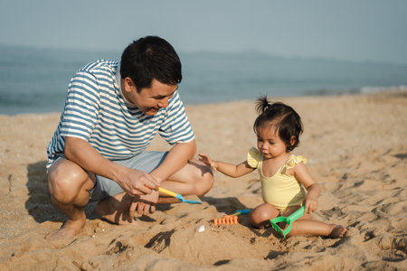 happy toddler baby girl playing sand toy with her father on the sea beachの写真素材