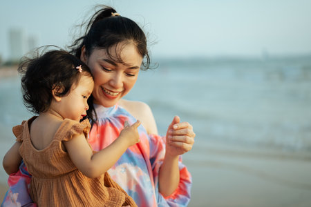 happy mother holding and talking toddler baby girl on the sea beachの写真素材