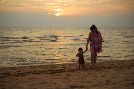 toddler baby girl walking with her mother on the sea beach at sunsetの写真素材