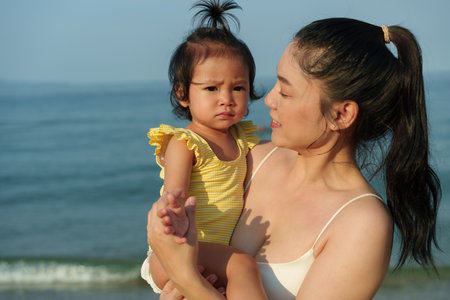 mother holding and talking toddler baby girl on the sea beachの写真素材