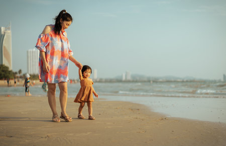 toddler baby girl walking with her mother on the sea beachの写真素材