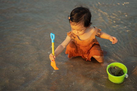 happy toddler baby girl playing toy and water on the sea beachの写真素材