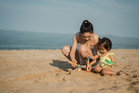 happy toddler baby girl playing sand toy with her mother on the sea beachの写真素材