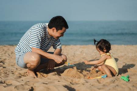 happy toddler baby girl playing sand toy with her father on the sea beachの写真素材