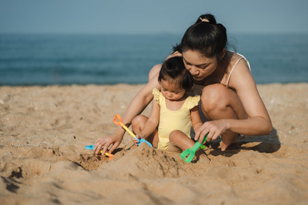 happy toddler baby girl playing sand toy with her mother on the sea beachの写真素材