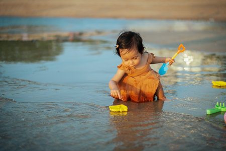 happy toddler baby girl playing toy and water on the sea beachの写真素材