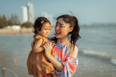 happy mother holding and talking toddler baby girl on the sea beachの写真素材