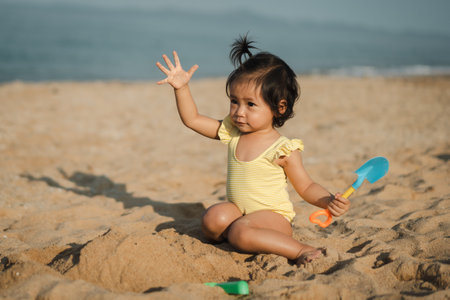 happy toddler baby girl playing sand toy on the sea beachの写真素材
