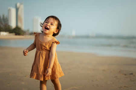 cheerful toddler baby girl laughing while standing on the sea beachの写真素材