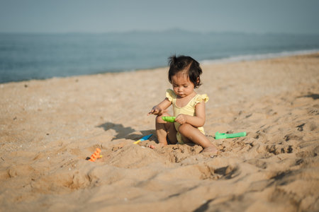happy toddler baby girl playing sand toy on the sea beachの写真素材