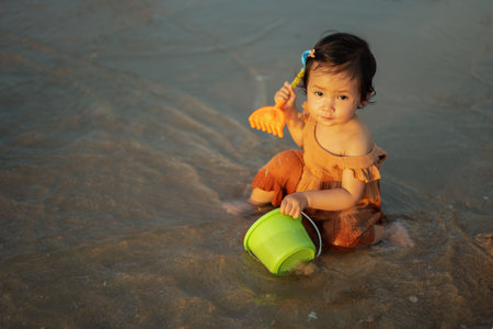 happy toddler baby girl playing toy and water on the sea beachの写真素材
