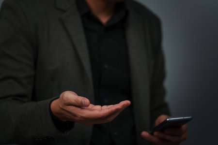 businessman with empty hand and open palm offering something while using a smartphoneの写真素材