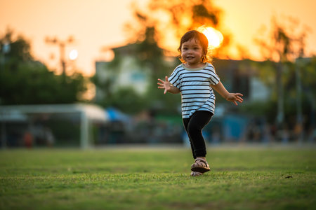 happy toddler girl running on grass field in the park at sunsetの写真素材