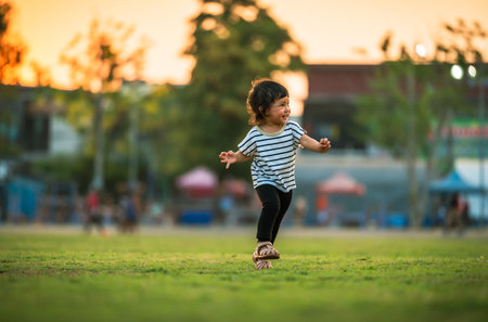 happy toddler girl running on grass field in the park at sunsetの写真素材