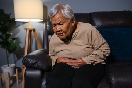 senior woman suffering from stomach ache  while sitting on a sofa in the living room at nightの写真素材