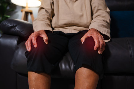 close up senior woman suffering from knee pain while sitting on a sofa in living room at nightの写真素材
