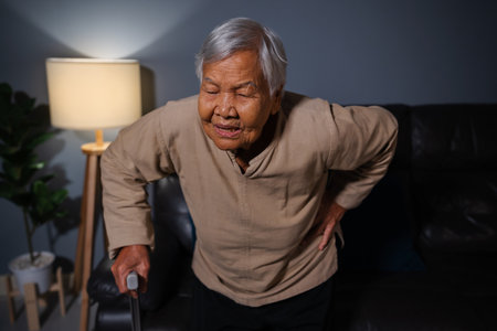 senior woman suffering from lower back pain in the living room at nightの写真素材