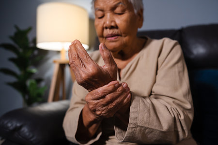 senior woman suffering from pain in wrist  while sitting on a sofa in living room at nightの写真素材