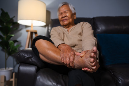 senior woman suffering from foot and ankle pain while sitting on a sofa in the living room at nightの写真素材