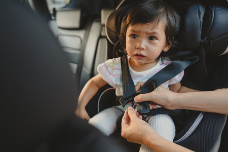 mother is fastening safety belt to crying toddler girl in a car seat, safety baby chair travellingの写真素材