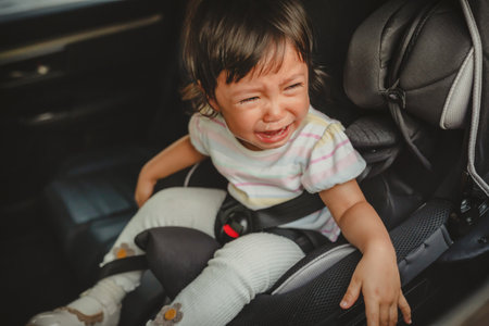 crying toddler girl sitting in a car seat, safety baby chair travellingの写真素材