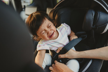 mother is fastening safety belt to crying toddler girl in a car seat, safety baby chair travellingの写真素材