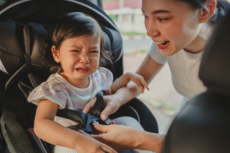 mother is fastening safety belt to crying toddler girl in a car seat, safety baby chair travellingの写真素材