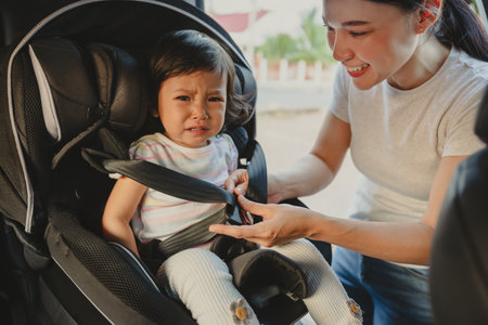 mother is fastening safety belt to crying toddler girl in a car seat, safety baby chair travellingの写真素材