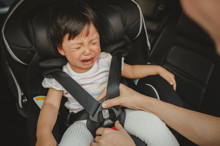father is fastening safety belt to crying toddler girl in a car seat, safety baby chair travellingの写真素材