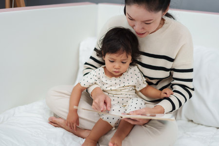 mother read story in the book for toddler baby on a bedの写真素材