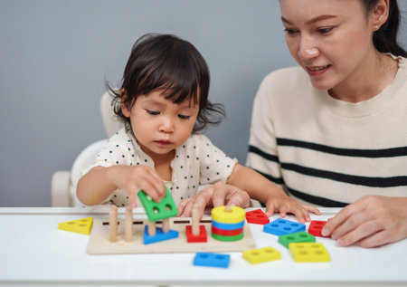 mother teaching her toddler baby girl to playing wooden educational geometric on the tableの写真素材