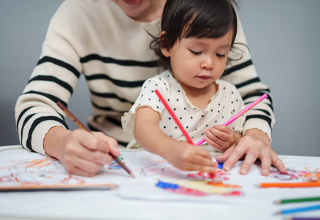 toddler baby training to drawing with colored pencil with mother helping on the tableの写真素材