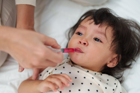 mother feeding a liquid medicine to baby girl by syringe. sick crying toddlerの写真素材