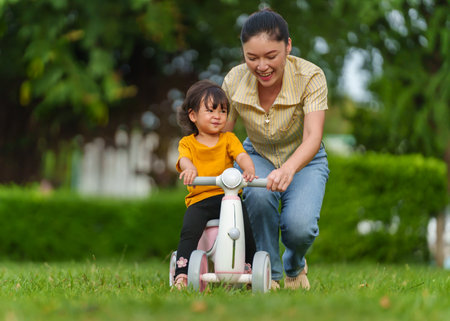 mother teaches her baby toddler girl rides a plastic motorcycle toy in the parkの写真素材