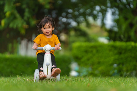 happy baby toddler girl rides a plastic motorcycle toy in the parkの写真素材